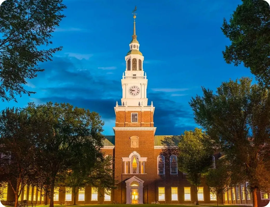 A clock tower and university building illuminated at dusk.